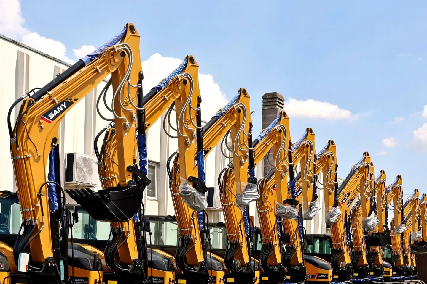 Row of new SANY excavators with yellow booms lined up outside a dealer building