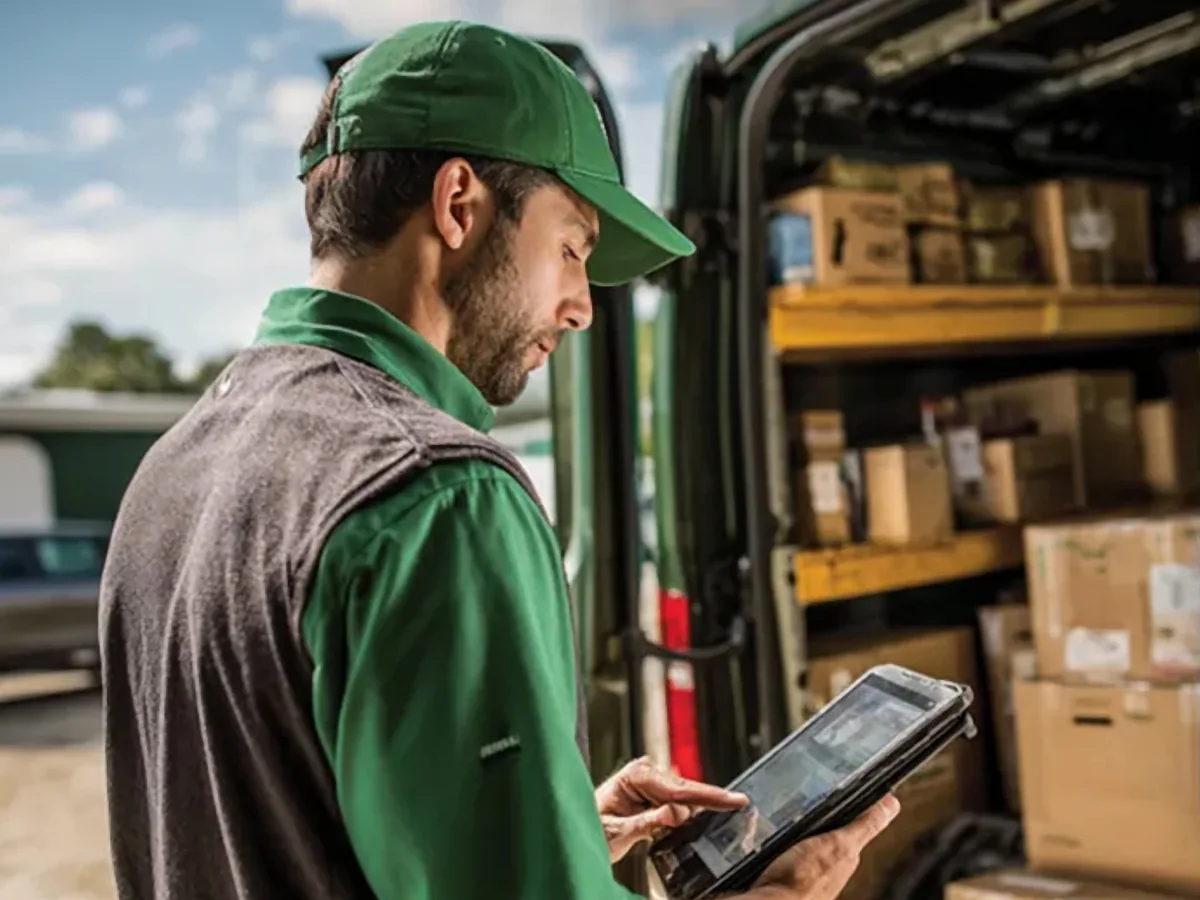 Delivery driver checking an order on a tablet beside a van loaded with packages