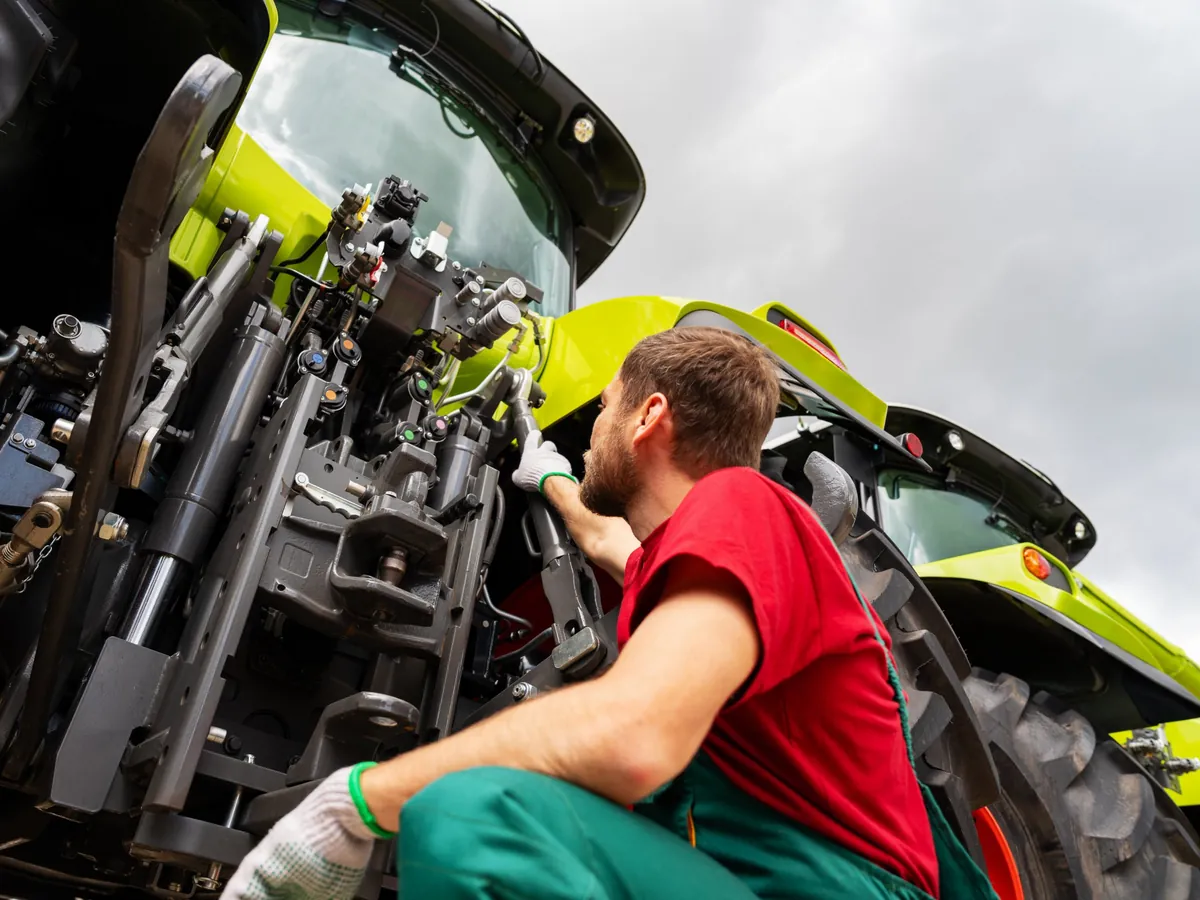Technician working on the rear hitch of a tractor in the field