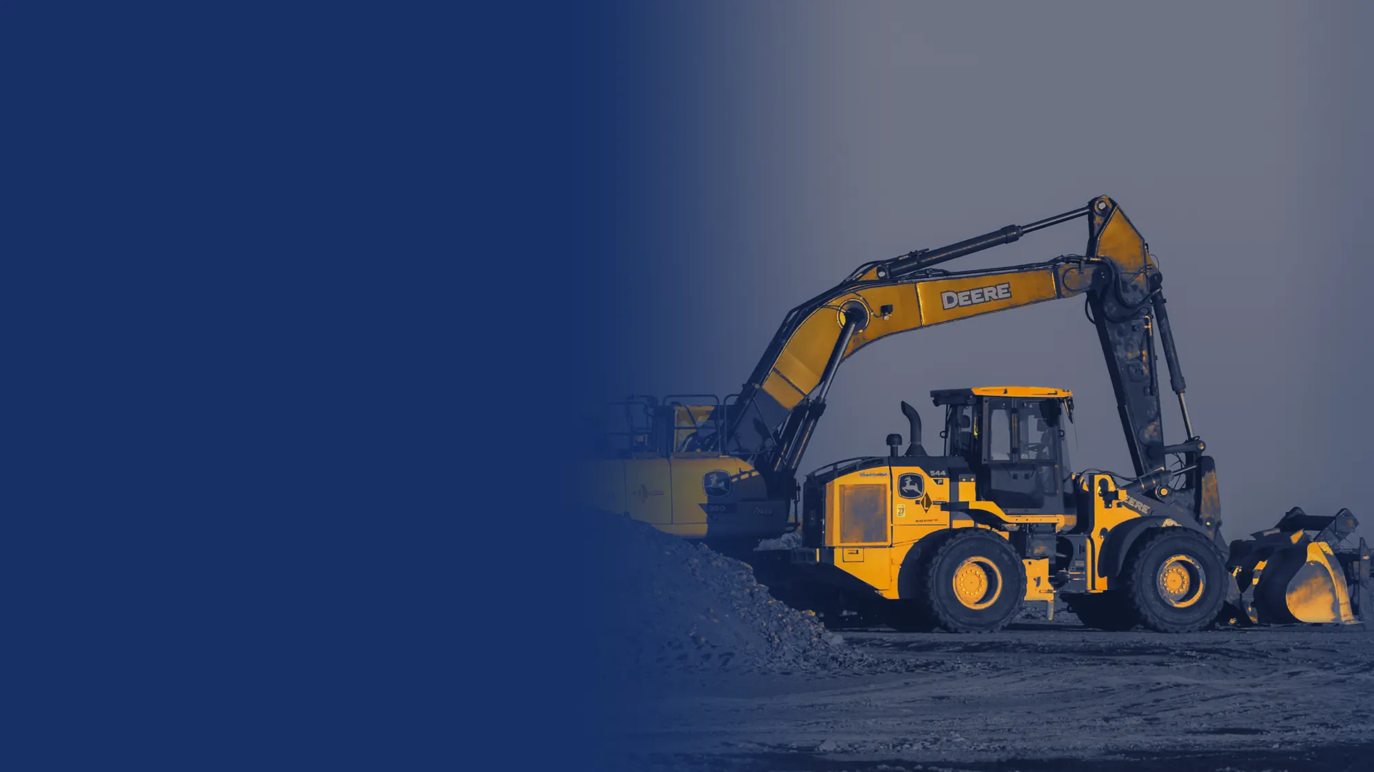 John Deere excavator and wheel loader beside a gravel pile at sunset