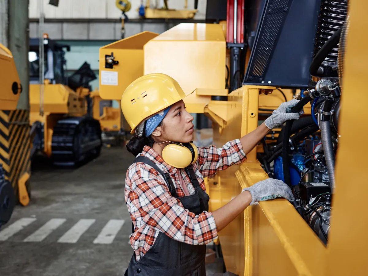 Technician in a hard hat working in a machine's engine bay