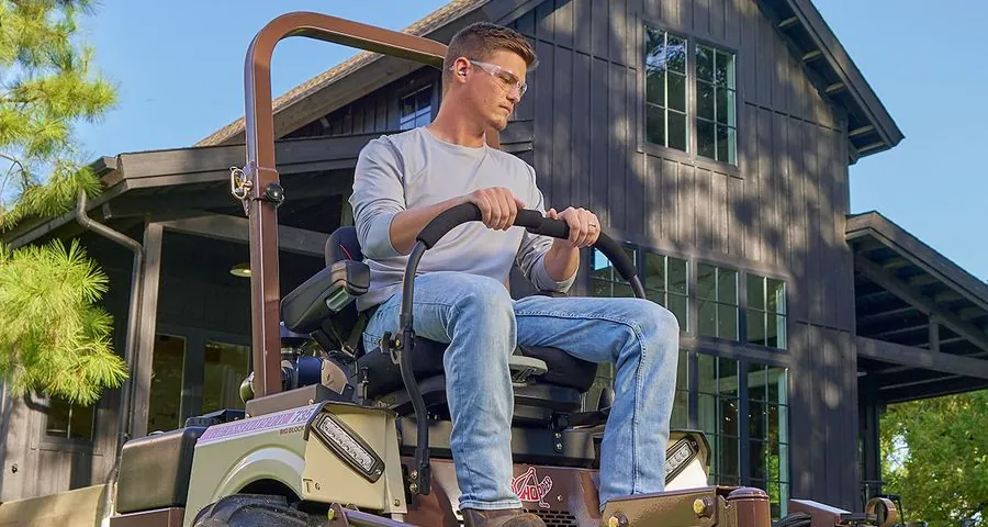 Operator on a Grasshopper zero-turn mower in a tree-lined park