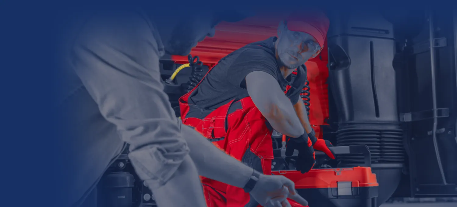 Truck technician with a toolbox talking with a service advisor at an open truck cab
