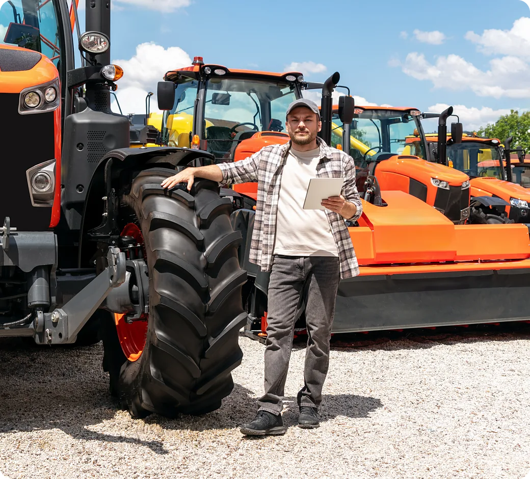 Customer on an equipment dealer lot holding a phone beside a row of orange tractors
