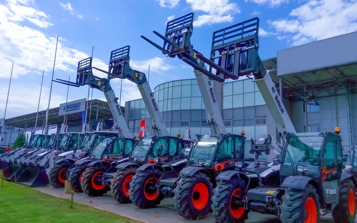 Row of Bobcat telehandlers with forks raised outside a dealership