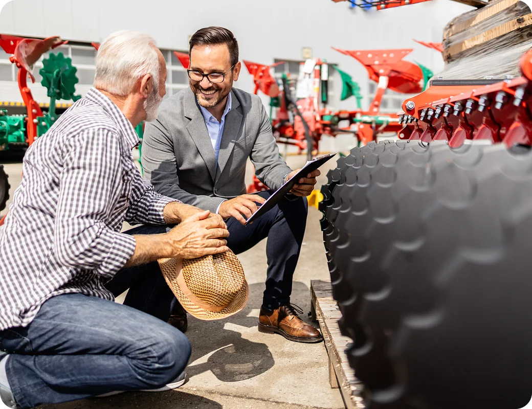 Salesperson going over a quote with a farmer next to a disc harrow on the lot