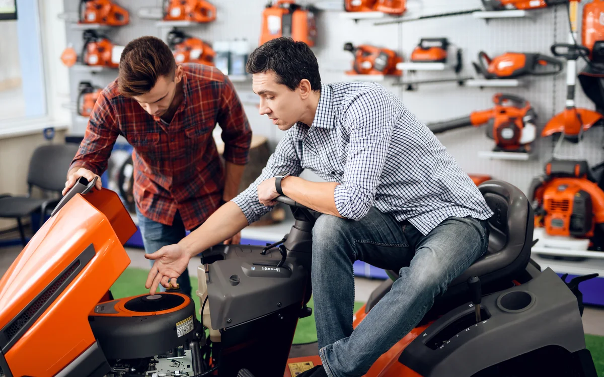 Salesperson showing a customer a riding mower in an outdoor power equipment store