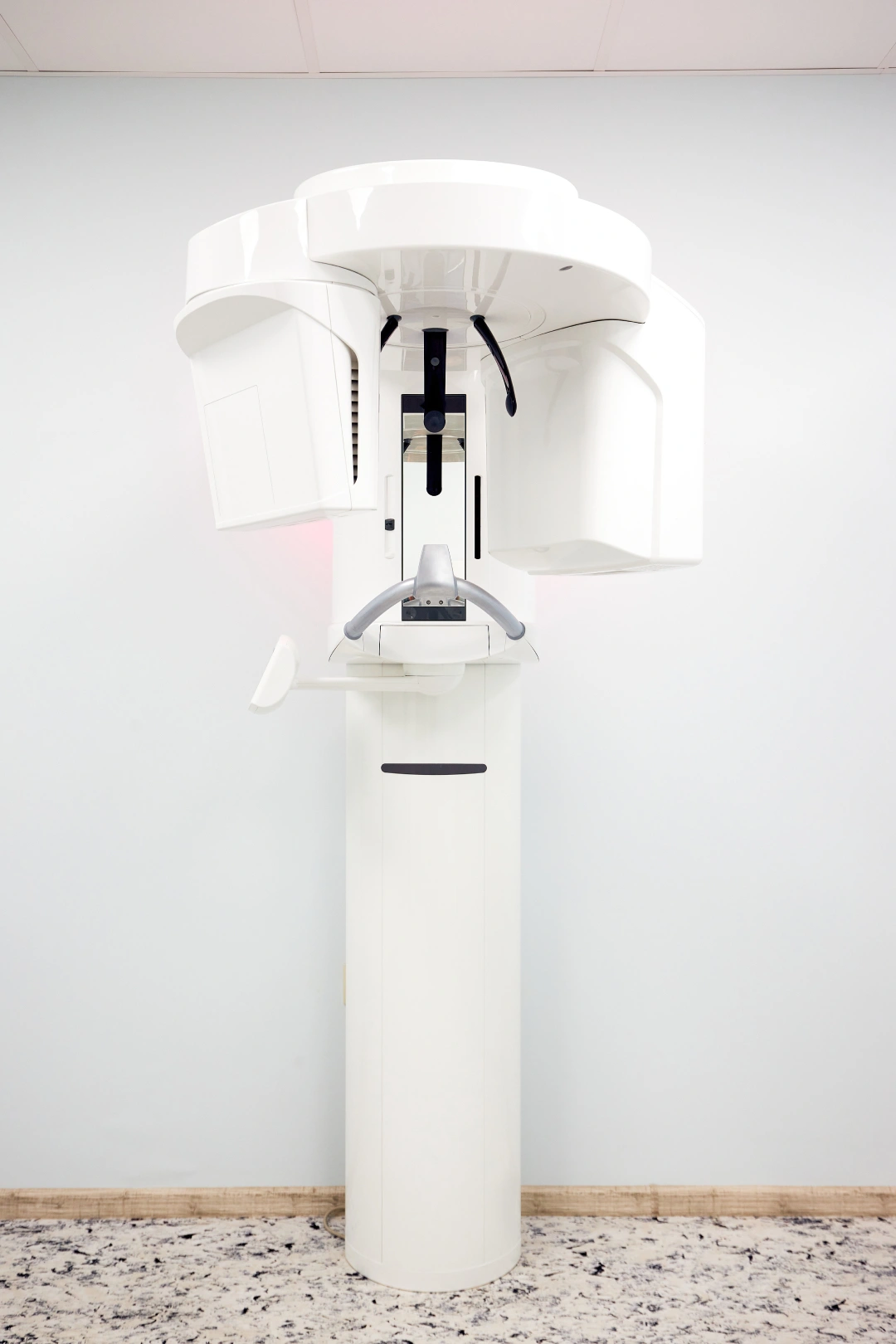 Modern white dental panoramic X-ray machine in a clean room with a white wall and patterned floor.