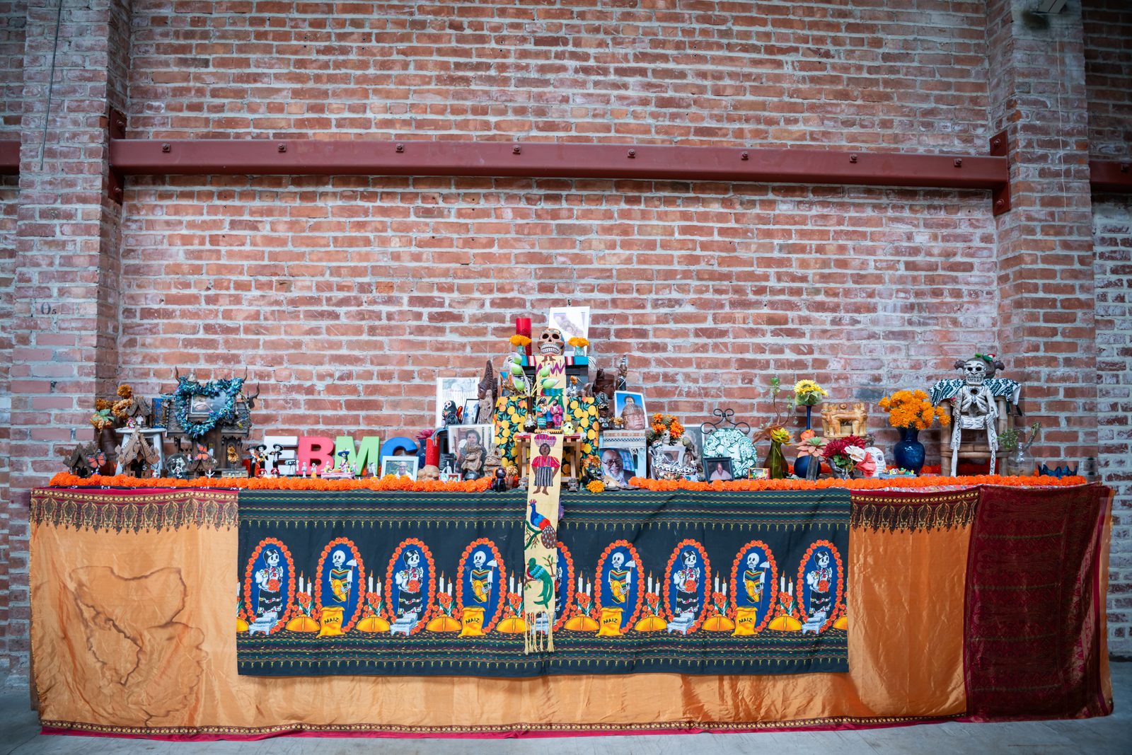 The altar at East Bay Meditation Center against a brick wall, covered with photographs, flowers, candles and figures on an embroidered orange cloth
