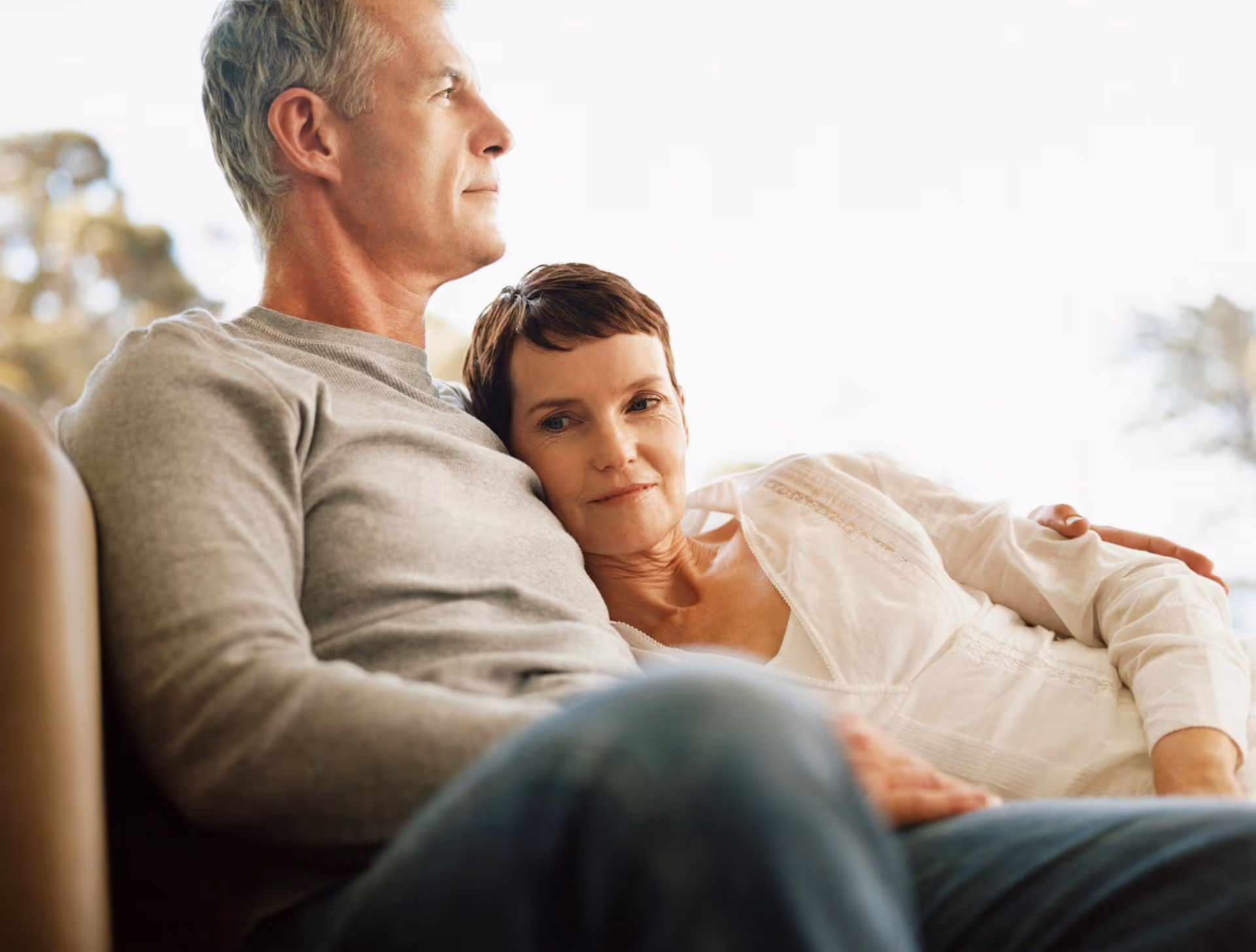 Middle-aged woman resting her head on a man's chest as they sit closely together on a couch.
