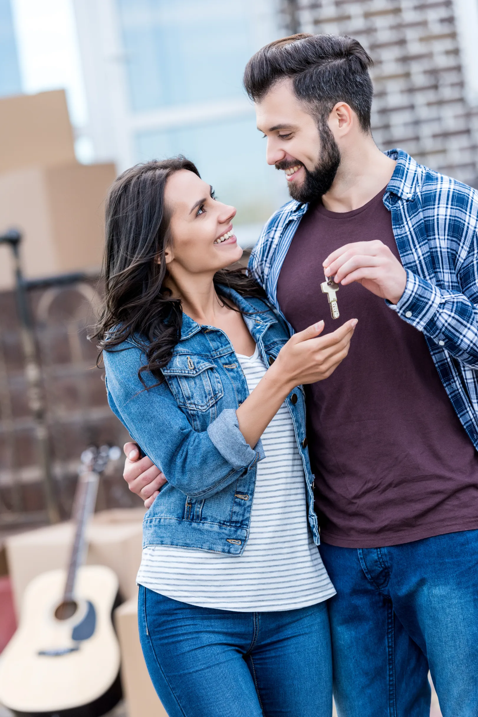 a couple looking at each other and holding keys indicating they bought a new home