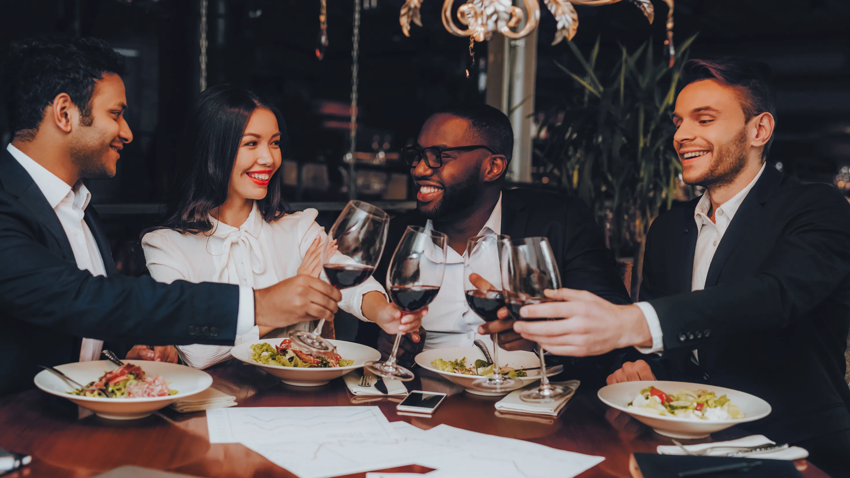 Group of friends dining at an upscale restaurant, toasting with glasses of red wine, and enjoying gourmet meals in an elegant setting in Folsom, CA.