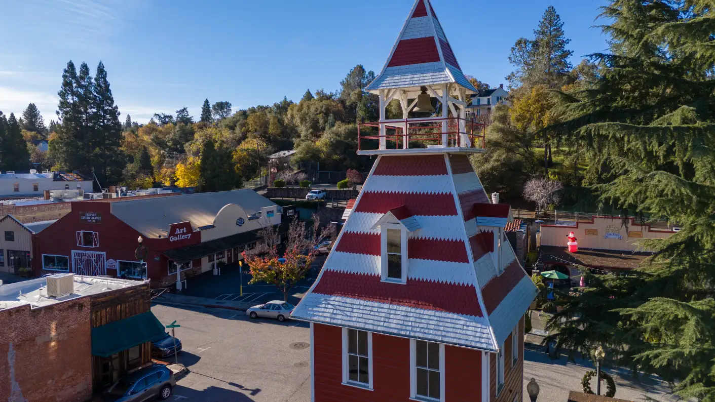 Historic firehouse with bell tower in downtown Auburn CA against a backdrop of shops and autumn trees.