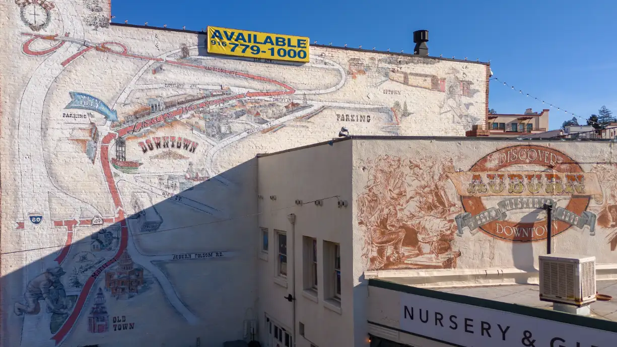 Mural on Auburn CA building showcasing the town's history and attractions with available real estate sign.