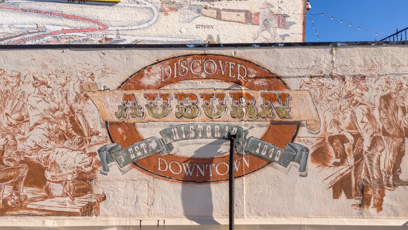 Close-up of the 'Discover Auburn' sign with a mural depicting the town's history, located in Auburn, CA.