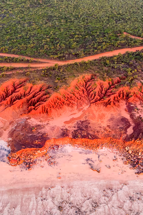 Aerial view of a landscape showing vibrant red soil formations with green vegetation and intersecting dirt roads.