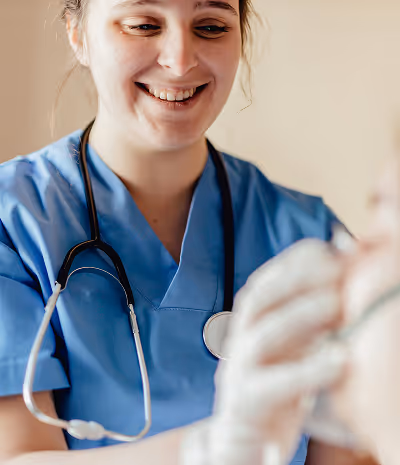 Smiling healthcare professional in blue scrubs with a stethoscope around her neck caring for a patient.