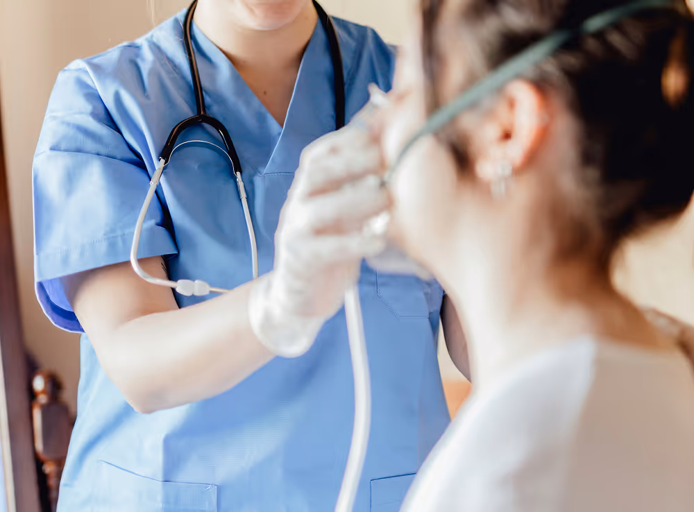 Healthcare professional in blue scrubs helping a patient with an oxygen mask.