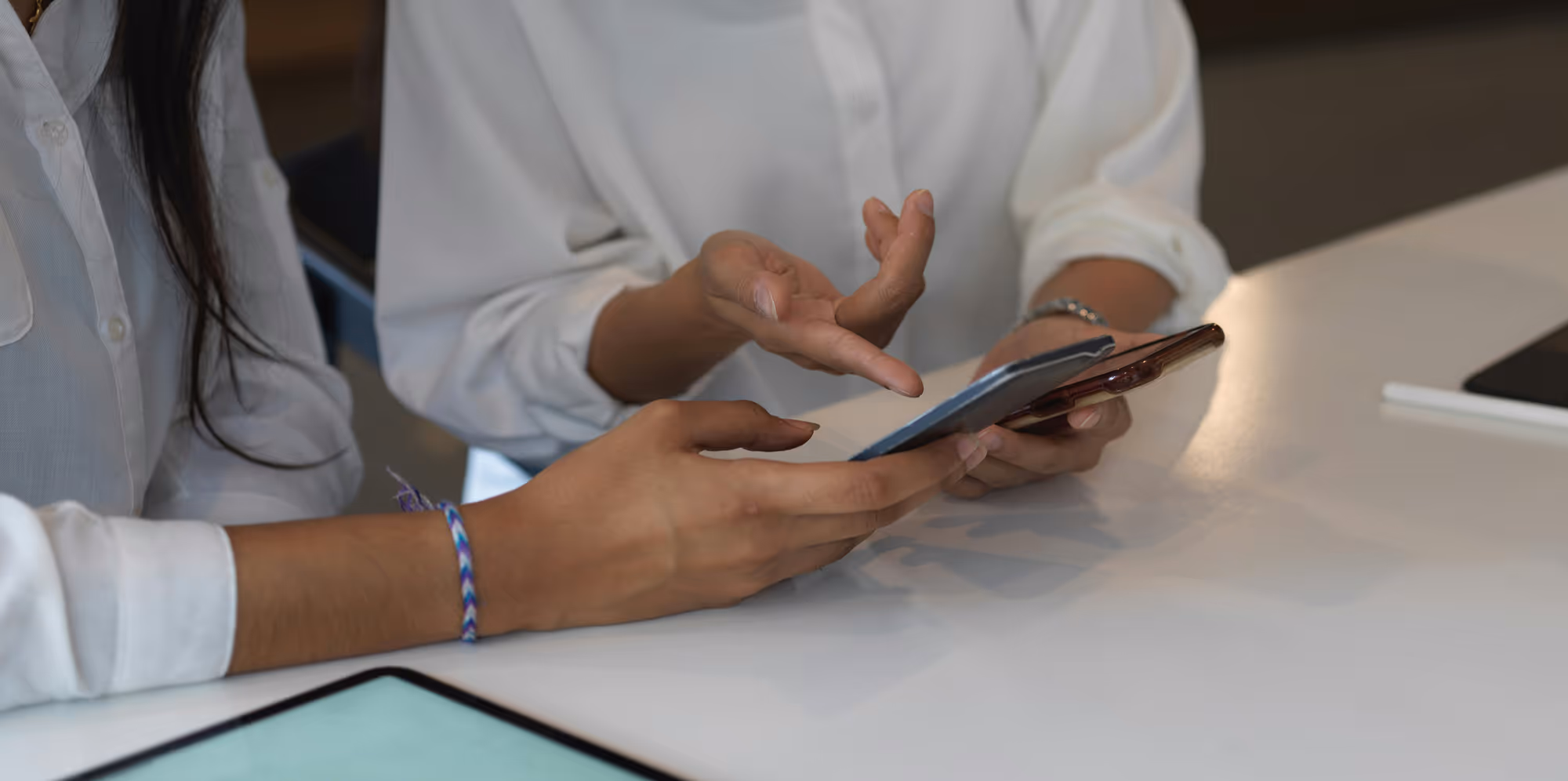 Two people in white shirts interacting with smartphones at a white table.