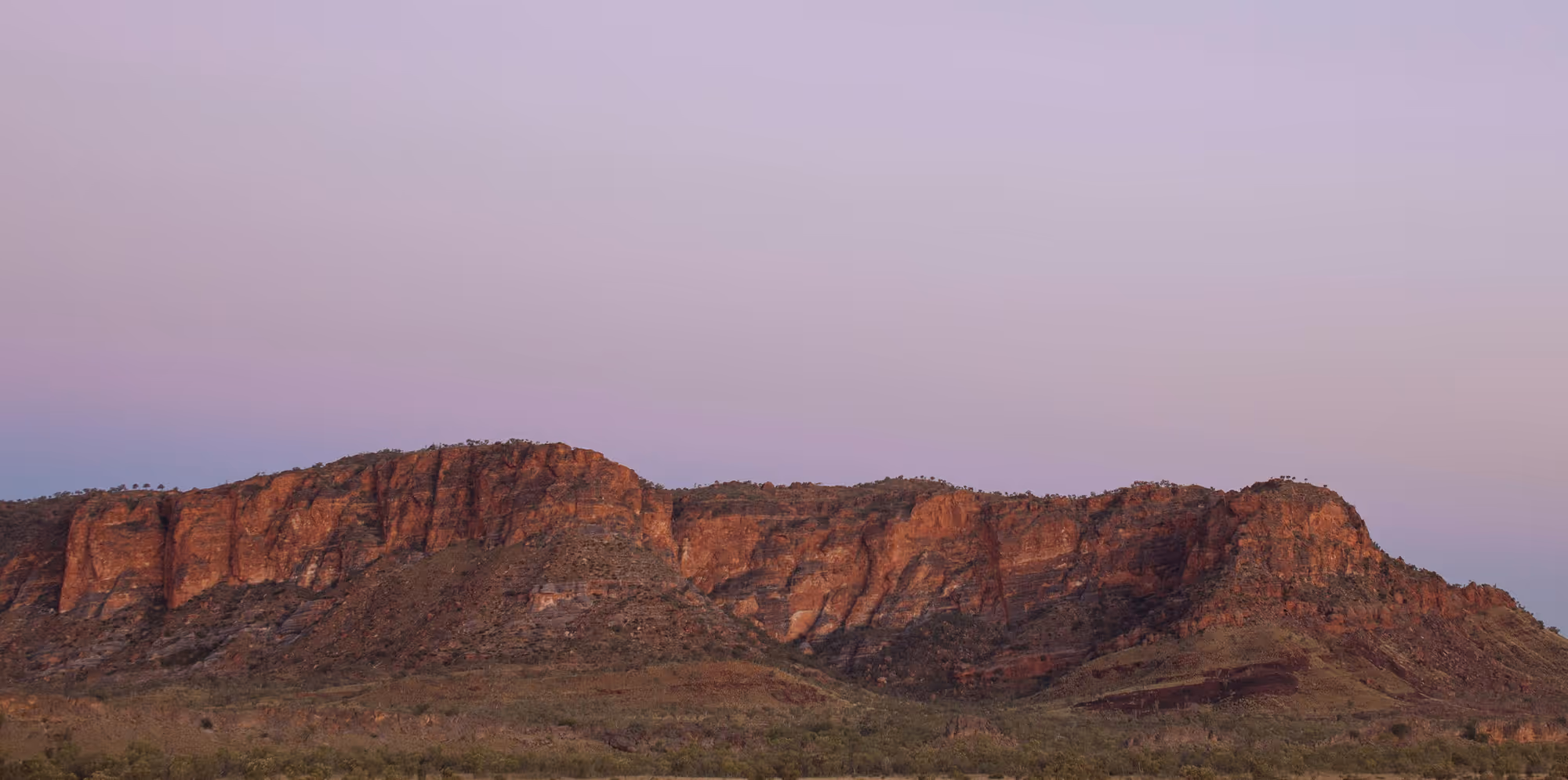 Red rocky mountain range under a clear purple and blue sky at dusk.