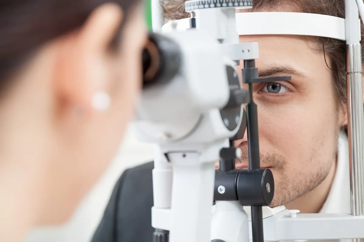 Man undergoing an eye exam using a slit lamp device at an optometrist's office.