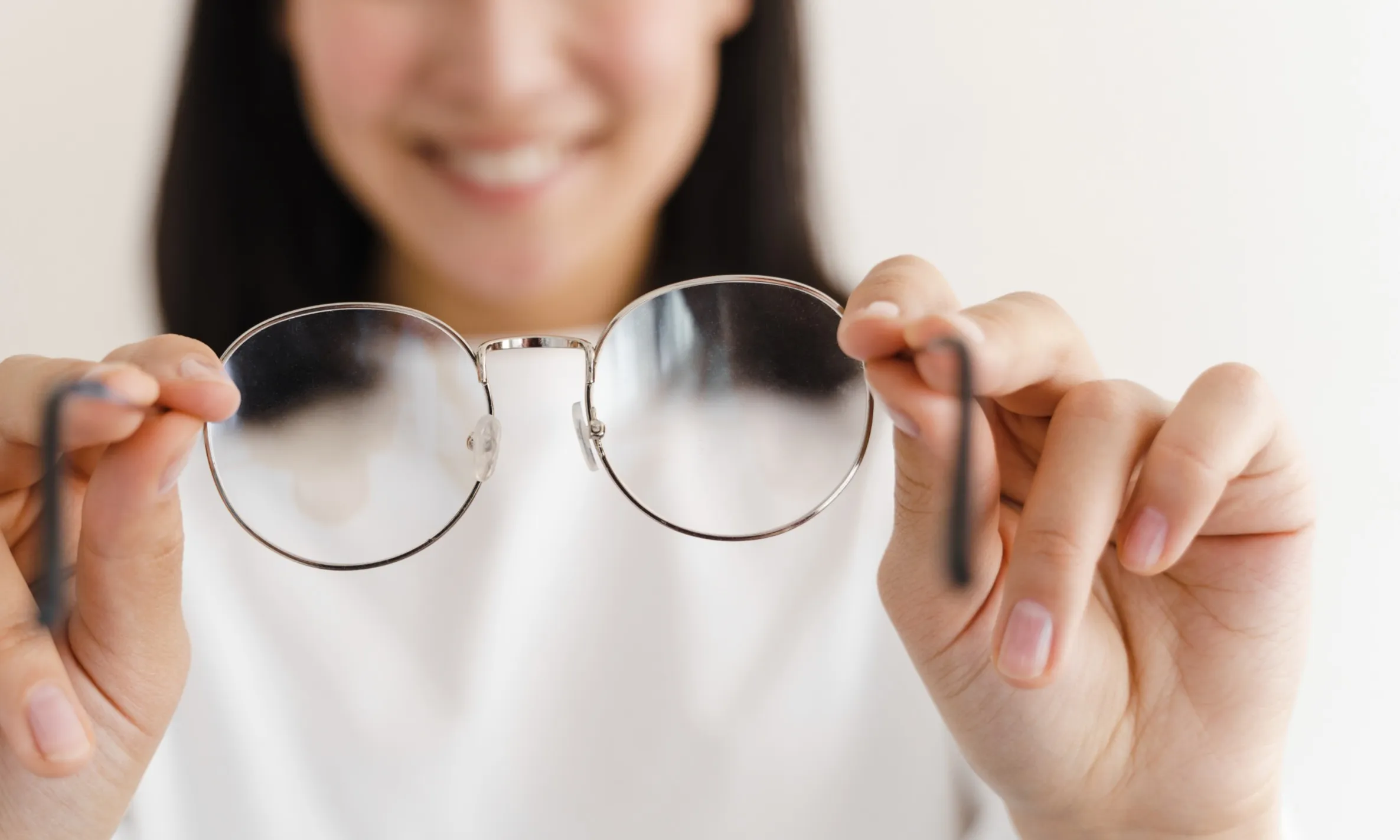 Smiling person holding round eyeglasses with metal frames toward the camera.