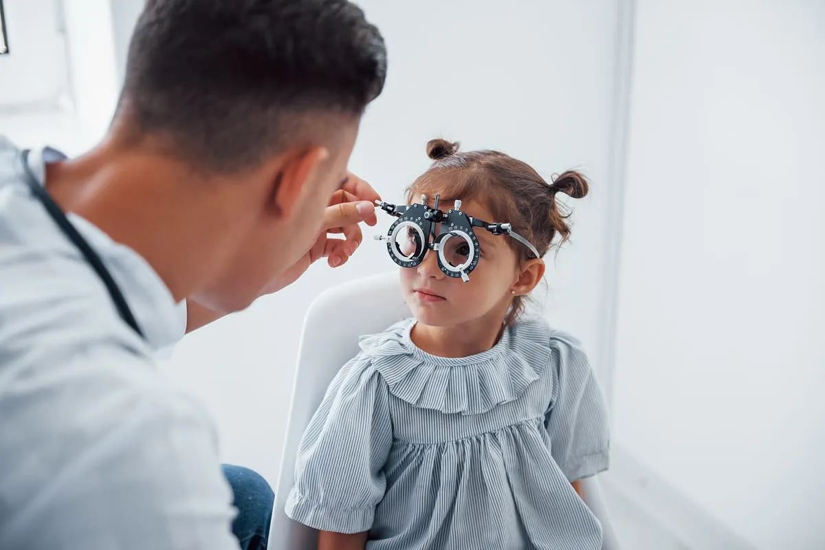 Young girl in a striped dress wearing a trial frame for an eye exam with an optometrist.