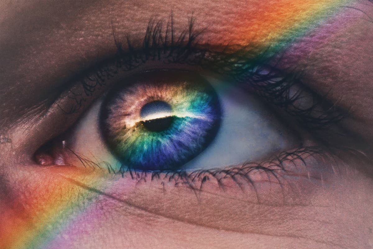 Close-up of an eye with a colorful rainbow reflection across the iris and surrounding skin.