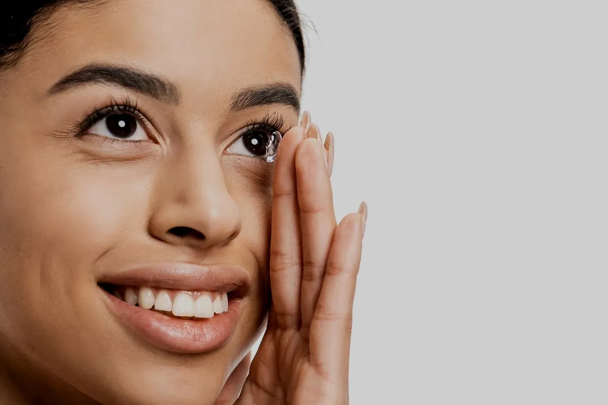 Woman smiling as she holds a contact lens near her eye for insertion.