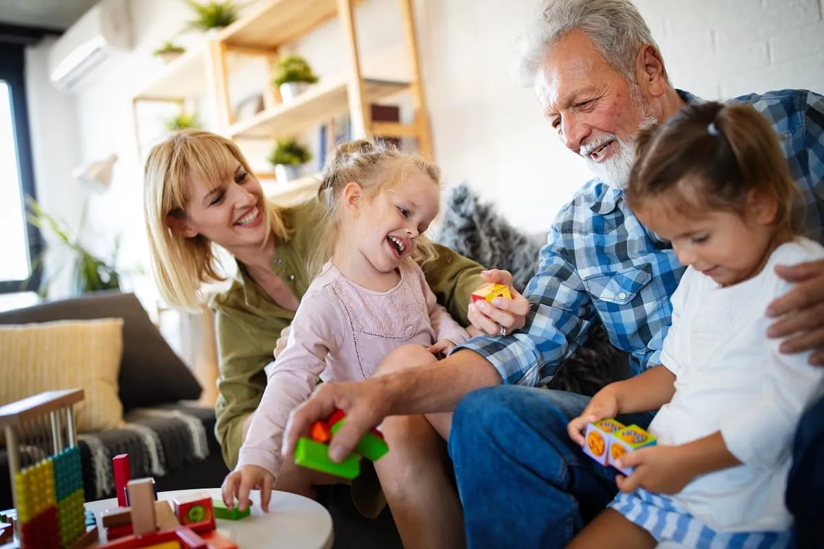 Grandparents and grandchildren playing with colorful blocks at a table in a cozy living room.