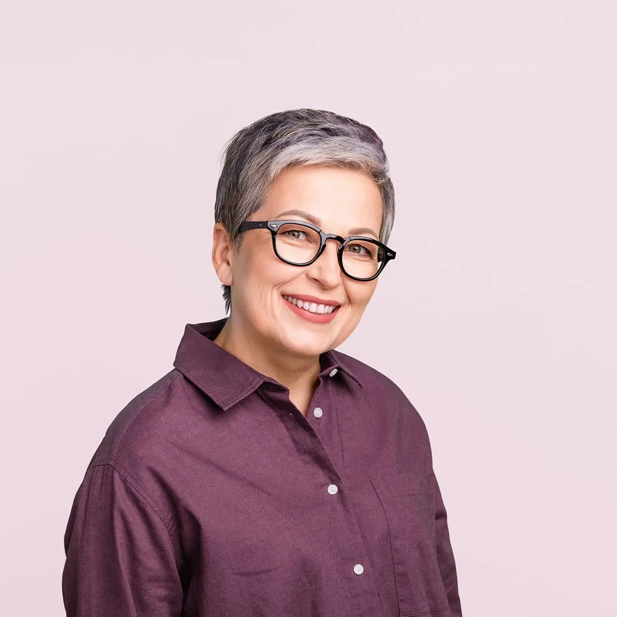 Smiling middle-aged person with short gray hair and black glasses in a purple button-up shirt.