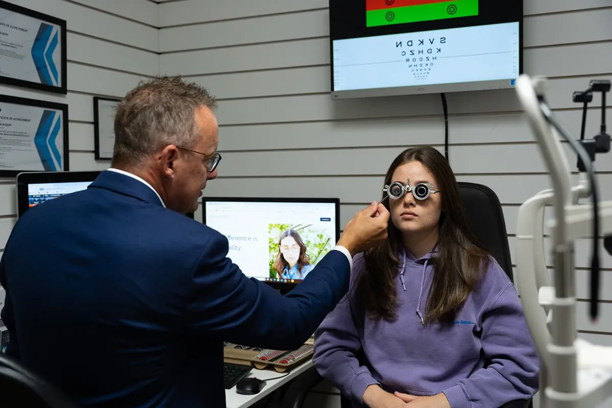 Optometrist adjusting a phoropter on a young woman during an eye exam in a clinic.