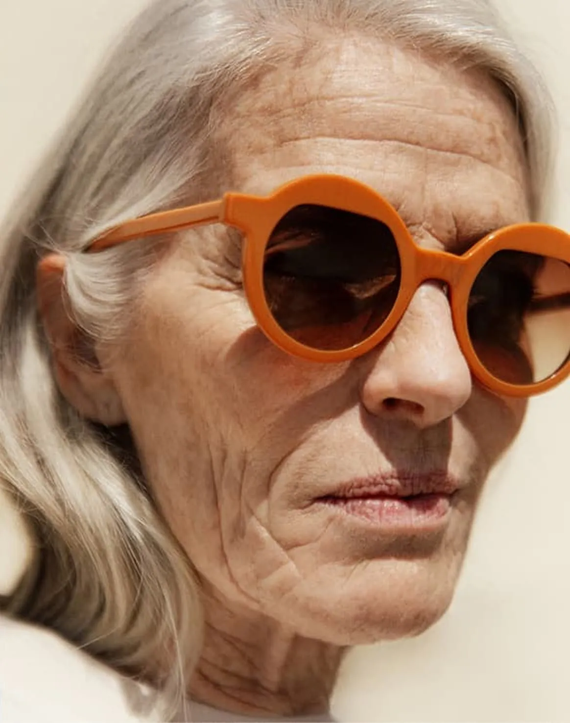 Close-up of an elderly woman with gray hair wearing round orange sunglasses.