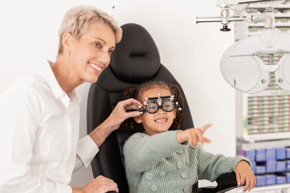 Child wearing an eye testing device pointing ahead while an optometrist adjusts the device.