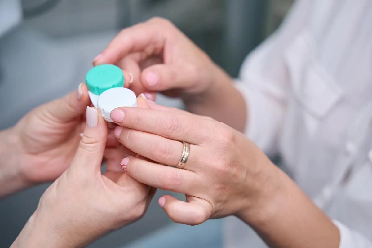 Close-up of two hands holding a small contact lens case with green and white lids.