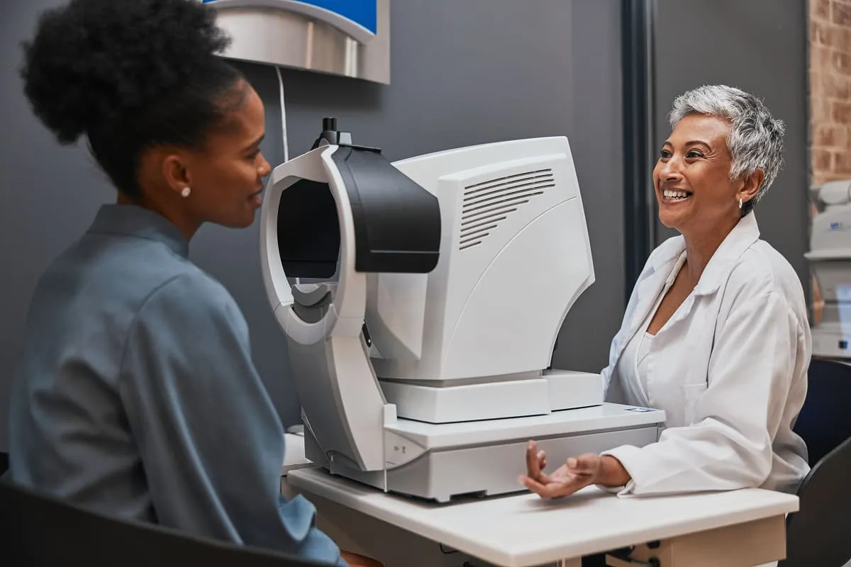 Smiling female optometrist conducting an eye exam with an autorefractor machine for a patient.