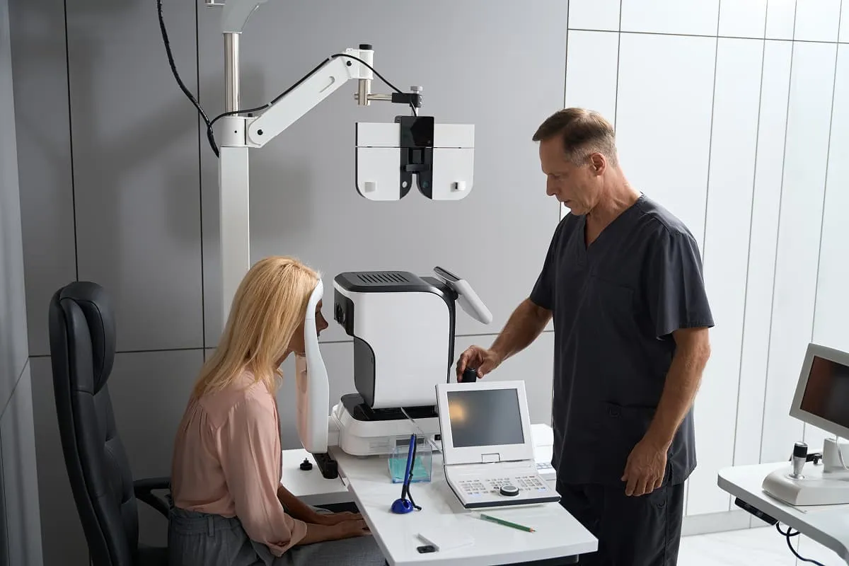 Optometrist conducting eye examination using digital equipment with a female patient seated at the machine.