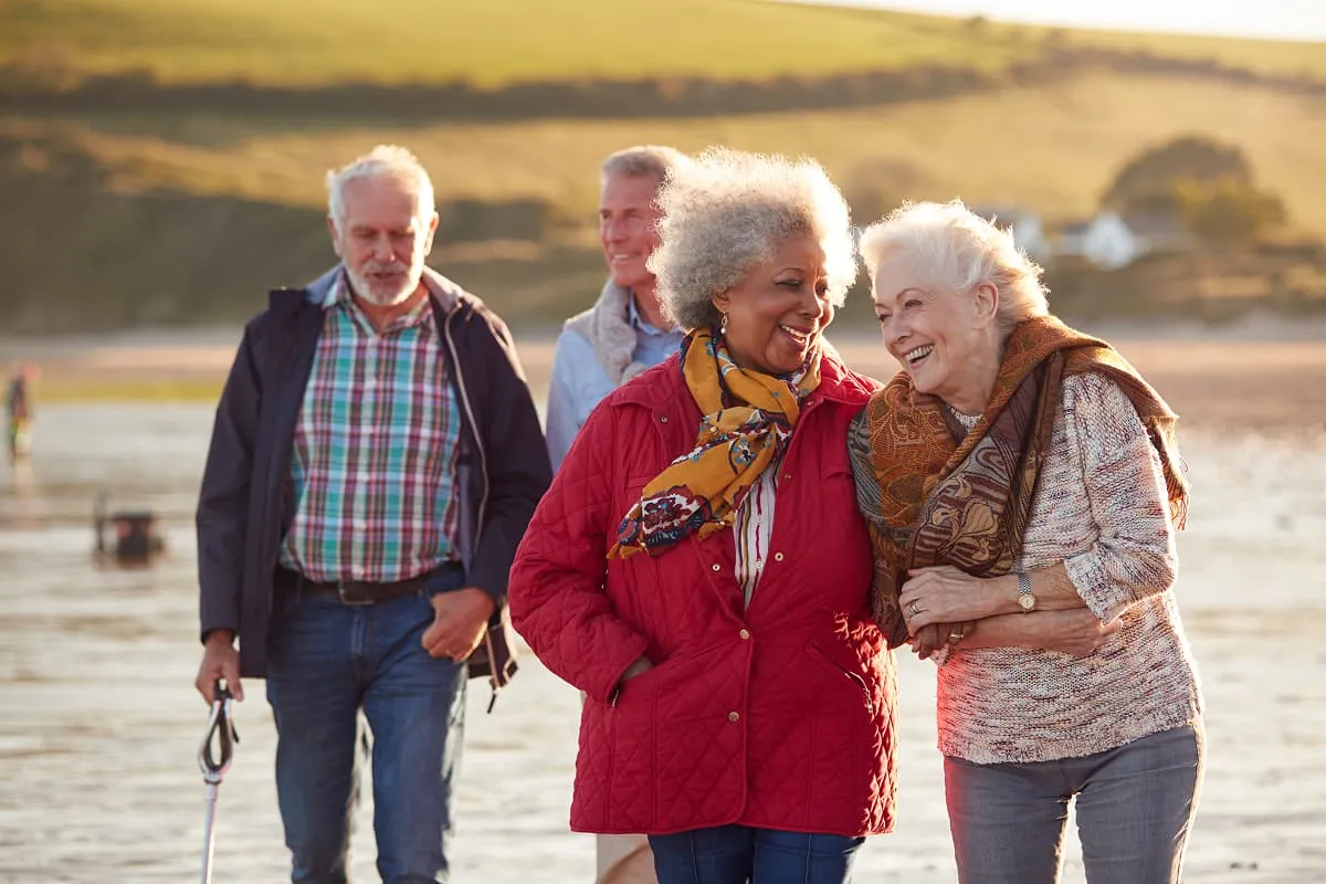 Group of older adults smiling and walking together along a beach