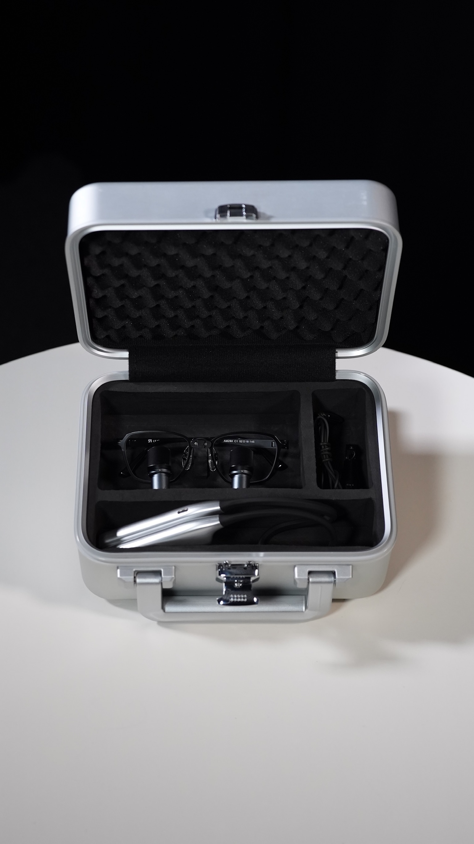 Open silver case containing a pair of black prismara ergonomic loupes and a prismara solis lights.