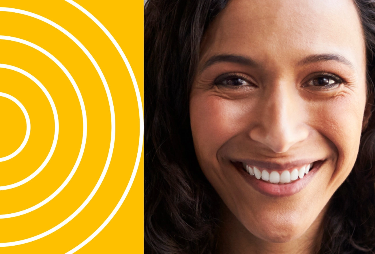 Woman with dark hair smiling beside white concentric circles on bright yellow background