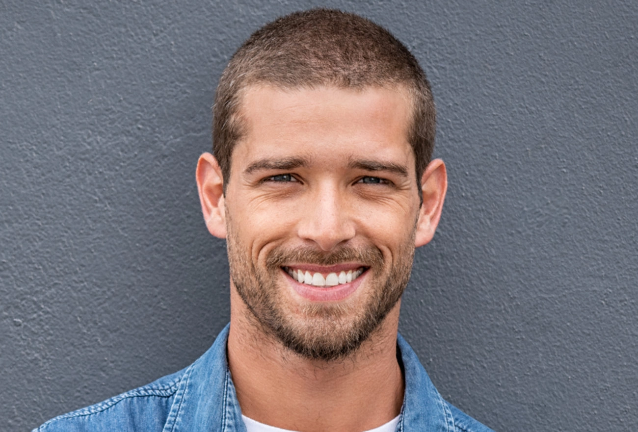 Smiling man with beard wearing blue denim shirt against gray background