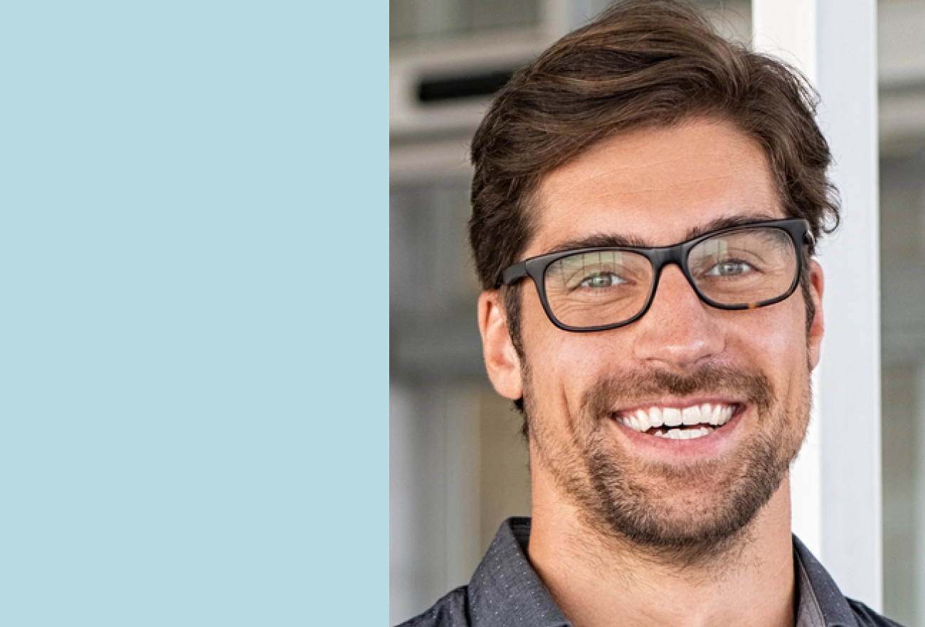 Man with glasses and beard smiling next to light blue background, split composition portrait