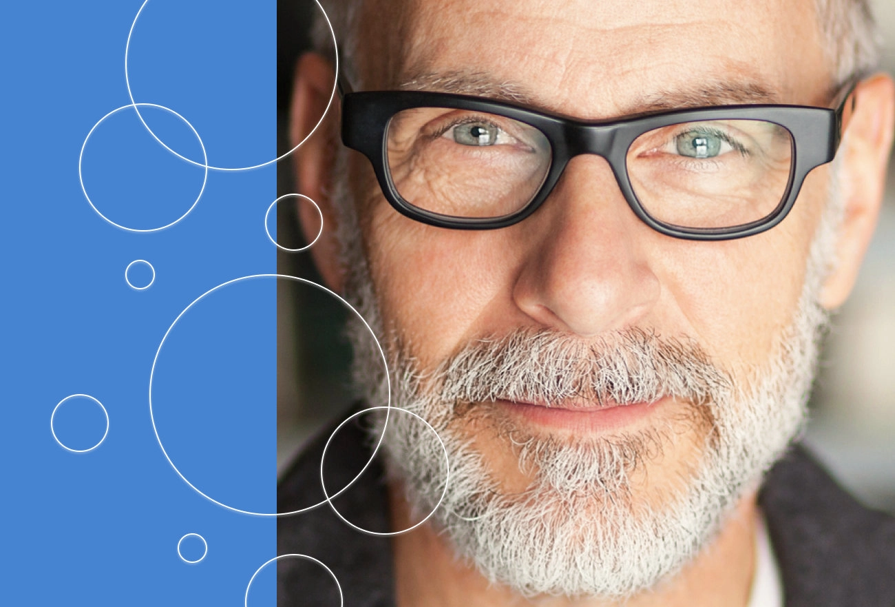 Older man with gray beard and black glasses next to blue background with white circular geometric pattern