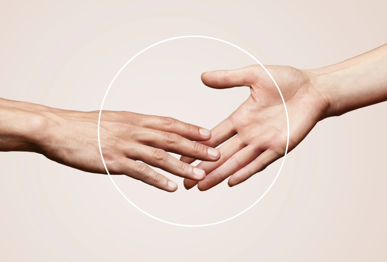 Two hands coming together with white circular outline on neutral background, teamwork concept