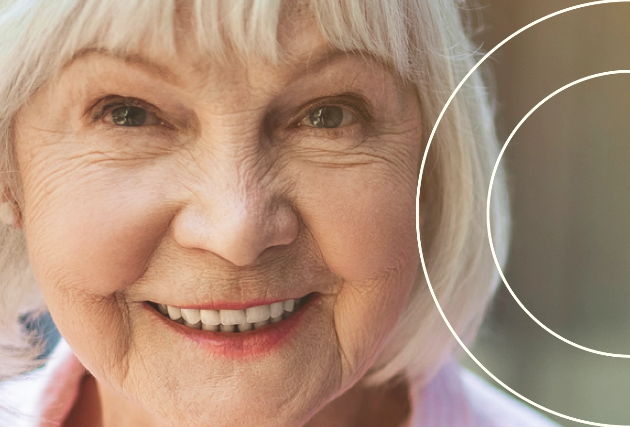 Smiling older woman with white hair and bangs, with white magnifying circles overlay on right side