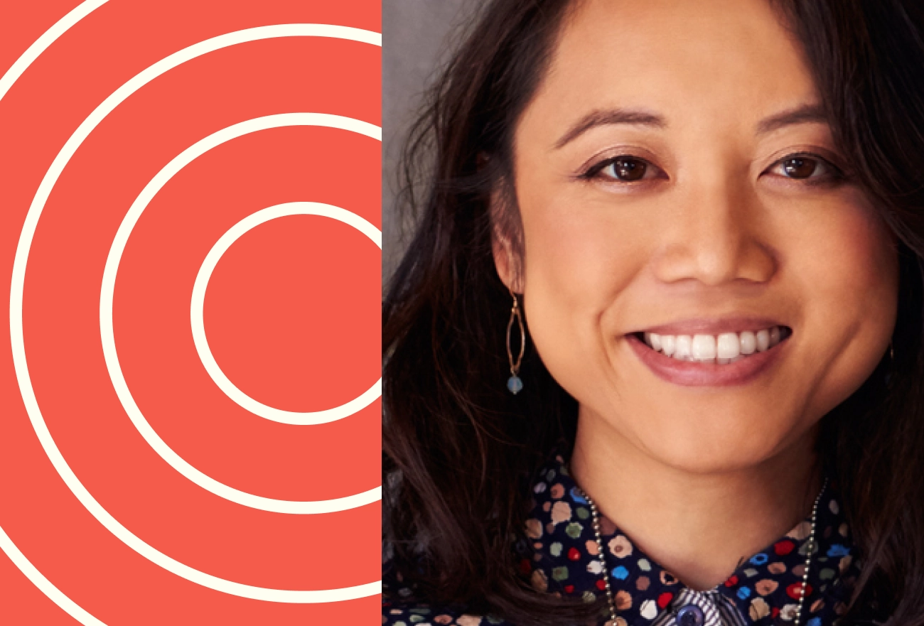 Smiling woman with black hair next to white concentric circles on coral background