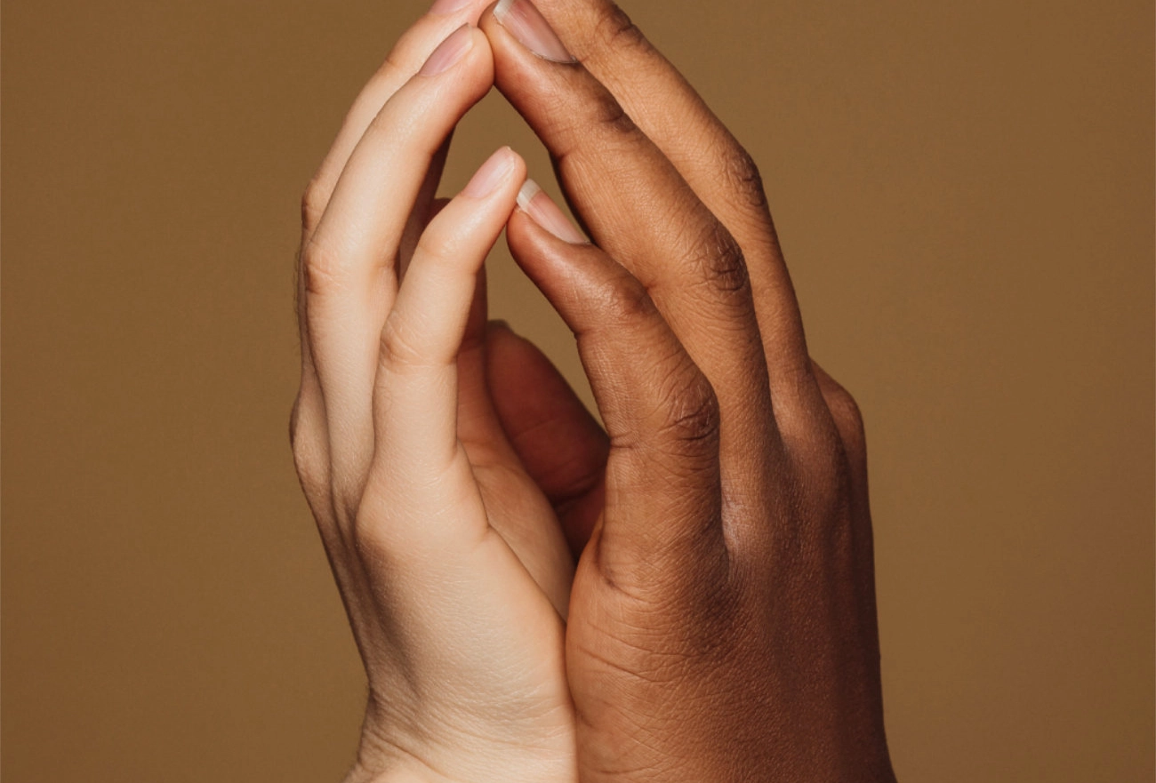 Two hands of different skin tones gently touching in gesture of care and connection against brown background