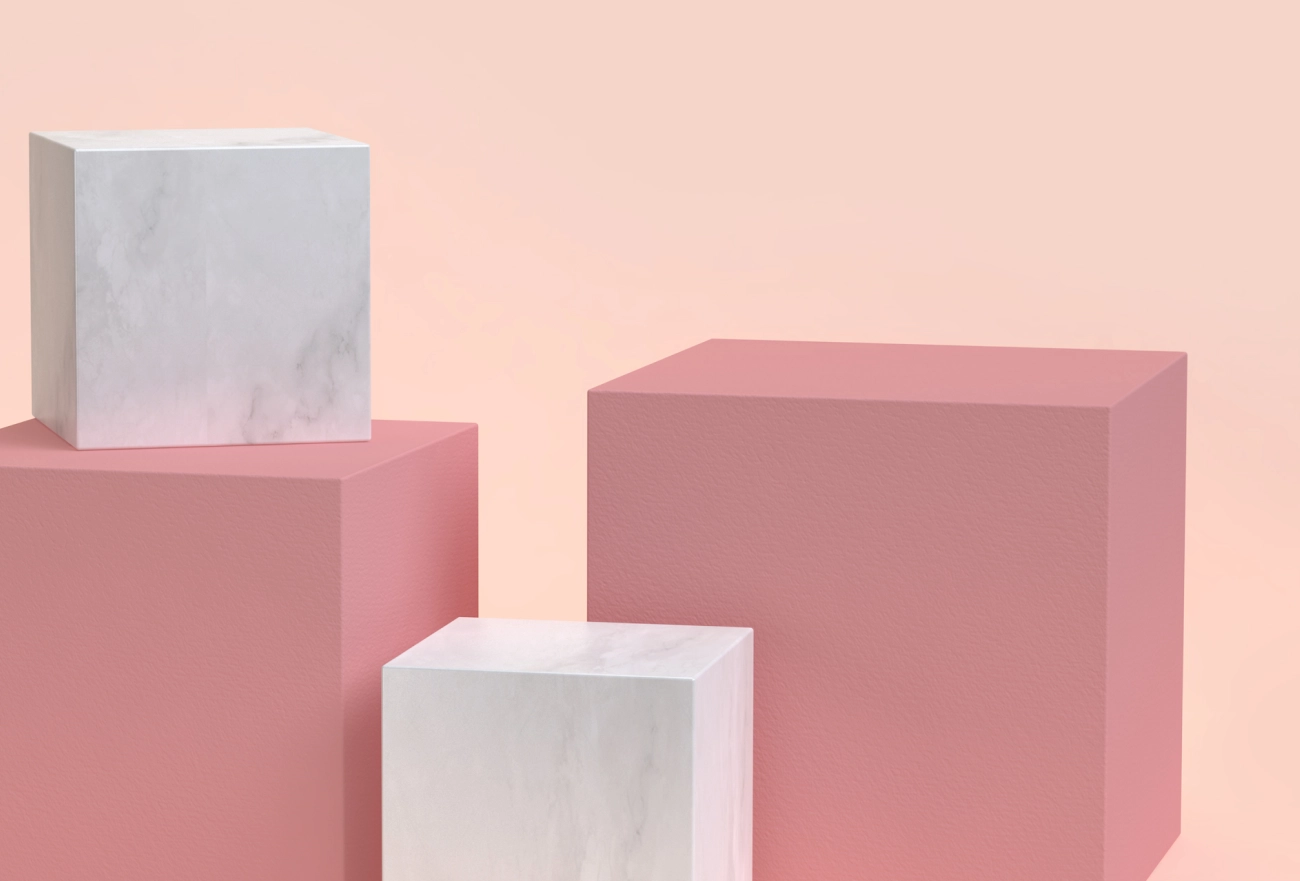 Three dimensional cubes in varying sizes with white marble and pink finishes on soft pink background