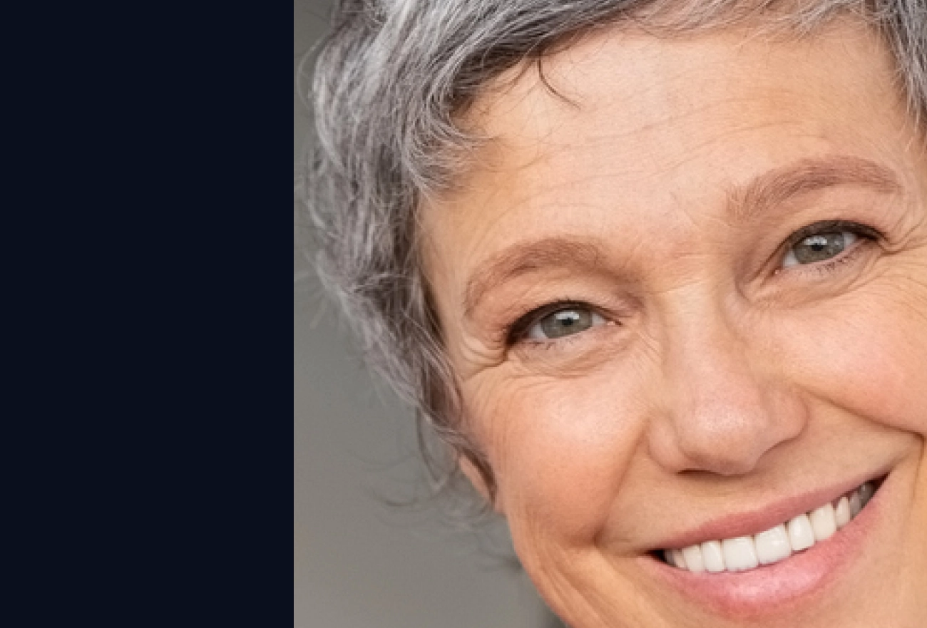 Older woman with gray hair smiling at camera next to dark navy section on left side