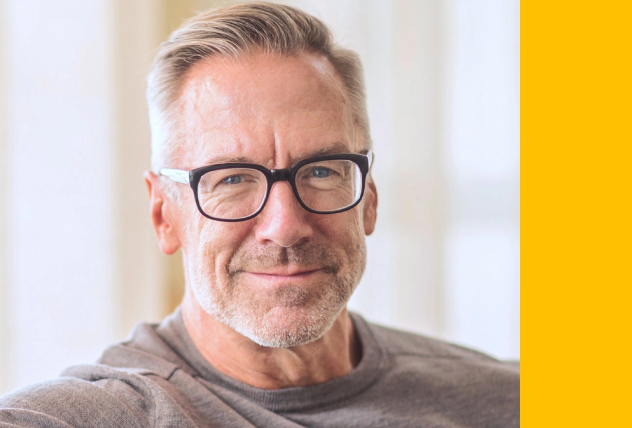 Man with glasses and beard in gray shirt against white and yellow background